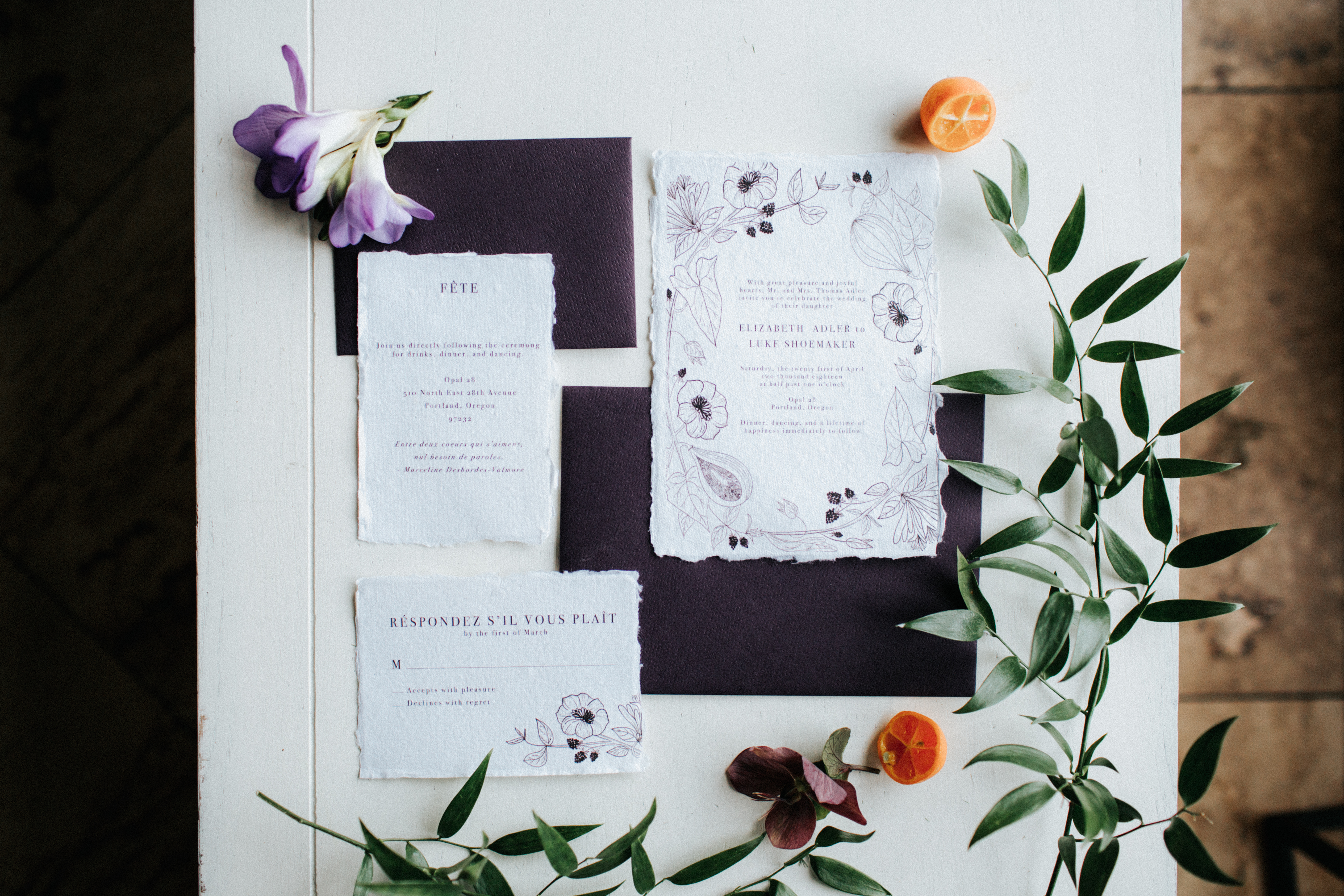 detail shot of wedding invitations with greenery, purple flowers, and oranges